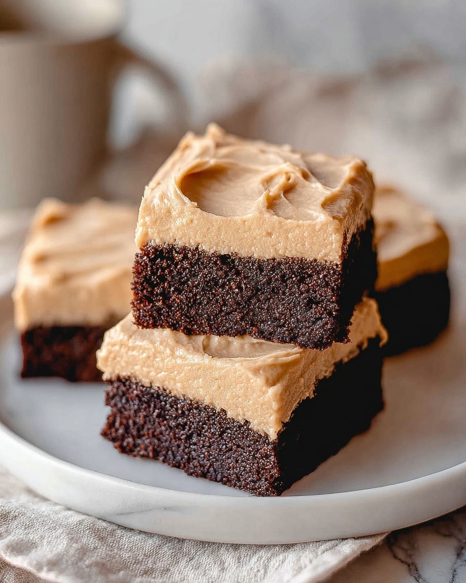 The image shows three square pieces of cake on a white plate, placed on a white marbled surface. Each piece has two layers: the bottom layer is thick, dark brown, and moist chocolate cake with a slightly crumbly texture, and the top layer is a smooth, thick, light beige frosting with visible swirls and soft peaks. The frosting covers the entire top surface of each cake square evenly. The background is softly blurred with neutral tones, highlighting the cake squares in the foreground. photo taken with an iphone --ar 4:5 --v 7