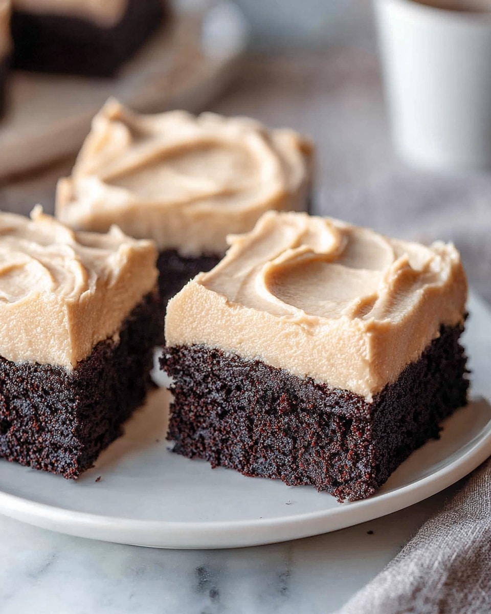 The image shows three square pieces of chocolate cake with a thick layer of light brown frosting on top. The cake layer is rich and dark, with a soft and moist texture, while the frosting looks smooth and creamy with slight swirls. The pieces are placed closely together on a white plate, which sits on a white marbled surface. The background is softly blurred, focusing on the cakes as the main subject. photo taken with an iphone --ar 4:5 --v 7