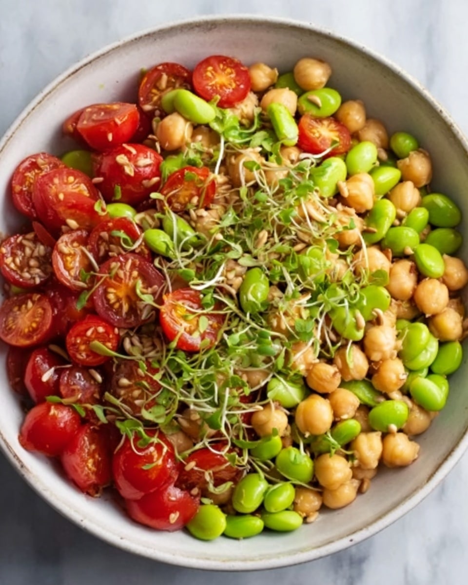 A white bowl filled with a colorful salad showing three main layers. The bottom layer is made of light green edamame beans scattered evenly. The middle layer consists of round, beige chickpeas mixed in. The top layer includes bright red cherry tomato halves and fresh green sprouts, sprinkled with seeds adding texture. The salad looks fresh and vibrant, all displayed on a smooth white marbled surface. Photo taken with an iphone --ar 4:5 --v 7