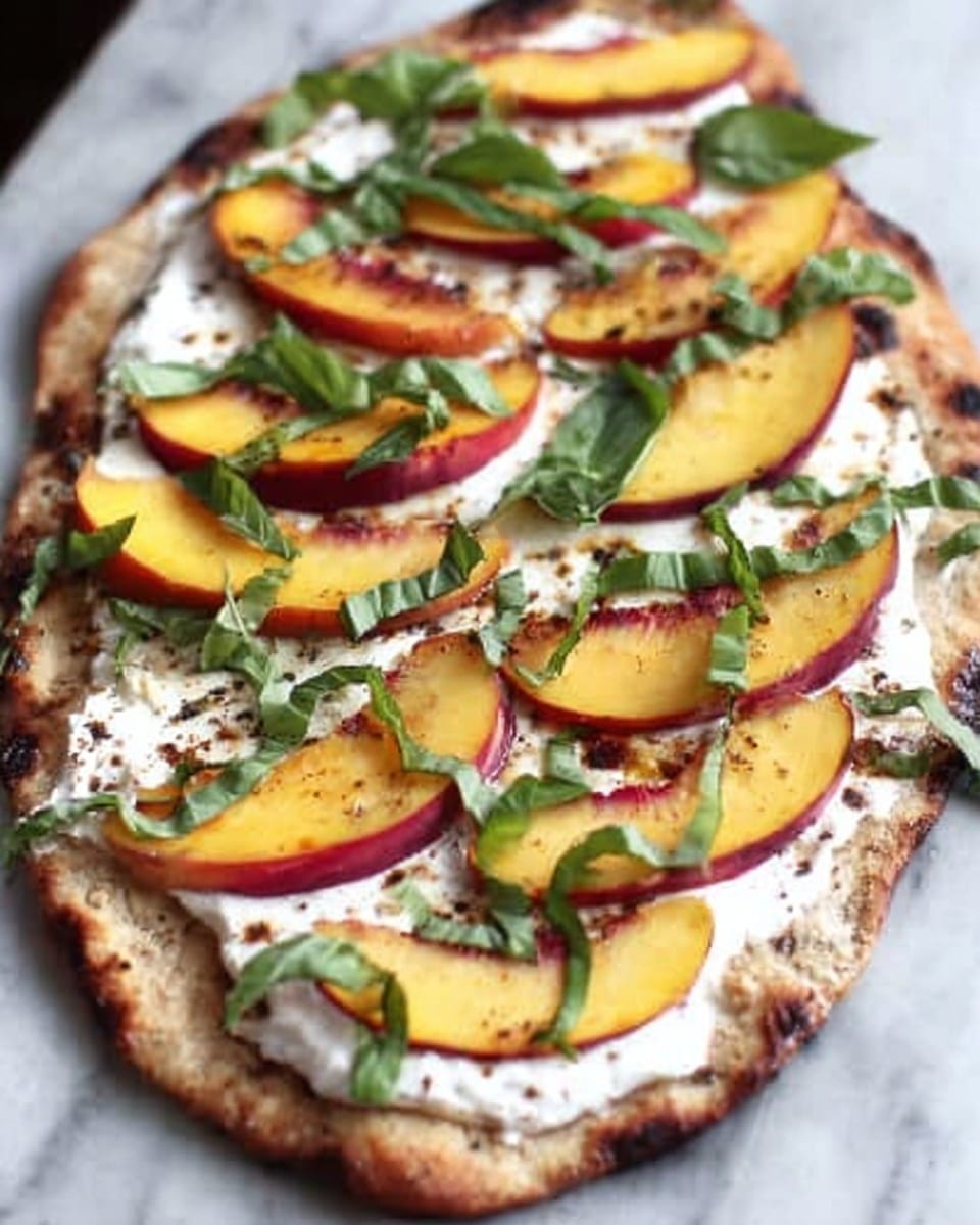 The image shows a flatbread topped with a creamy white spread covering the whole surface. Slices of yellow and red peach are evenly placed in a single layer on top of the cream. Thin strips of fresh green basil leaves are sprinkled over the peaches, adding color contrast. The flatbread crust is golden brown with some charred spots, and the whole dish is set on a white marbled surface. photo taken with an iphone --ar 4:5 --v 7