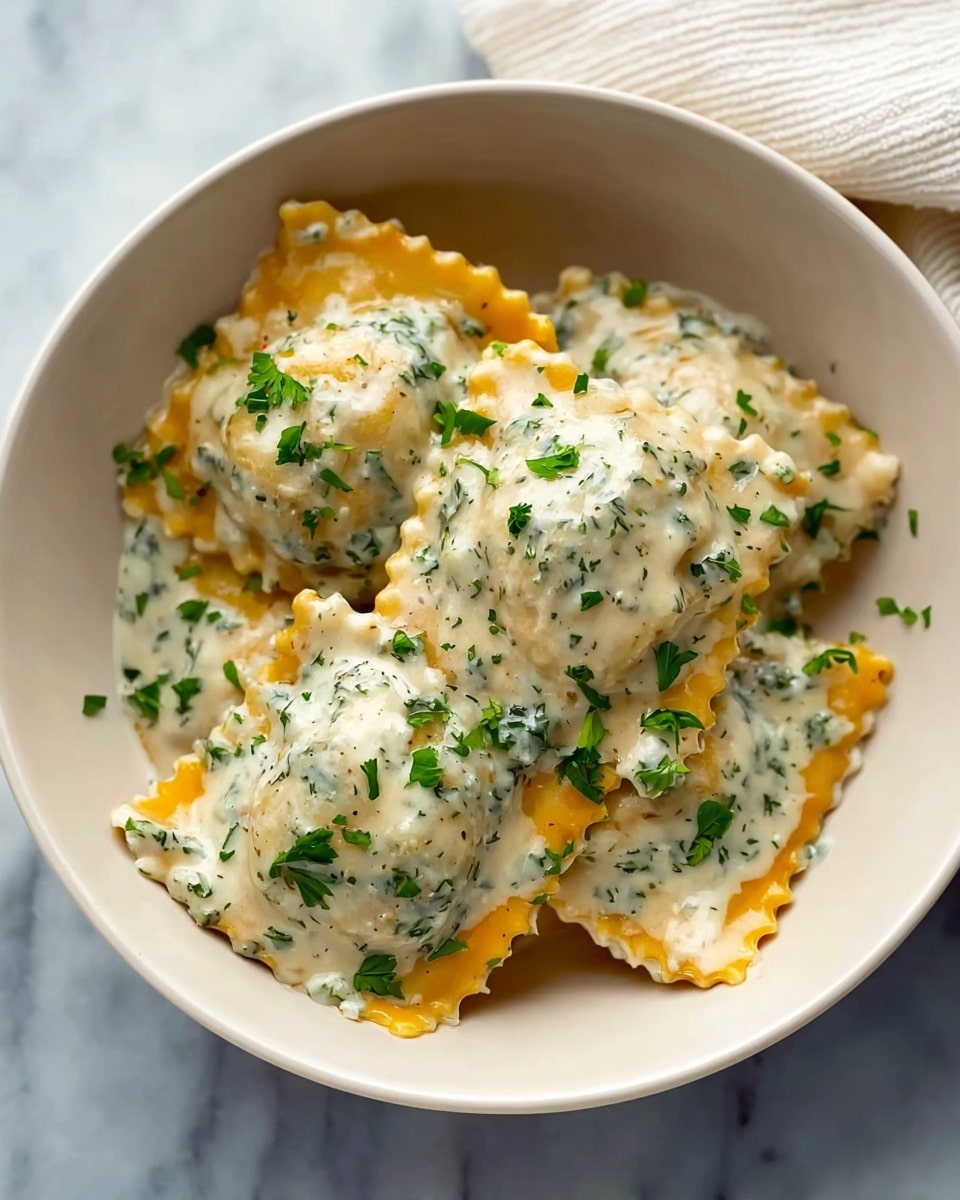 The image shows a white bowl filled with four large square ravioli pieces. Each ravioli has a golden-orange pasta layer, covered generously with a creamy white sauce mixed with finely chopped green herbs. Small fresh chopped parsley pieces are scattered on top of the ravioli and sauce, adding a bright green color contrast. The bowl sits on a white marbled texture surface with a white cloth napkin partially visible in the upper right corner. photo taken with an iphone --ar 4:5 --v 7
