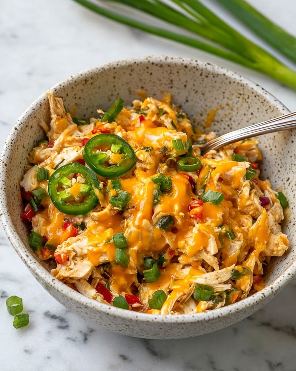 The image shows a white rectangular baking dish filled with a layered casserole. The top layer is a mix of shredded chicken and rice, with small pieces of diced red tomatoes and green onions scattered throughout. Bright green jalapeño slices sit evenly across the surface, adding contrast to the yellowish, cheesy, and slightly browned texture beneath. The edges of the dish have some browned bits from baking, adding a rustic look. The whole dish is sitting on a white marbled surface. photo taken with an iphone --ar 4:5 --v 7
