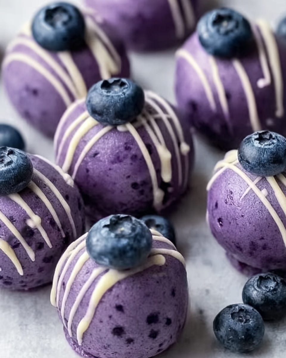 The image shows small round purple treats with a smooth, slightly shiny surface, each decorated with thin white lines drizzled on top, and a single fresh blueberry placed right in the middle of the top layer. The treats have a uniform size and are arranged loosely on a white marbled surface, with a few extra blueberries scattered around them, adding a fresh touch. The purple color of the treats has small darker specks throughout, giving them texture. photo taken with an iphone --ar 4:5 --v 7