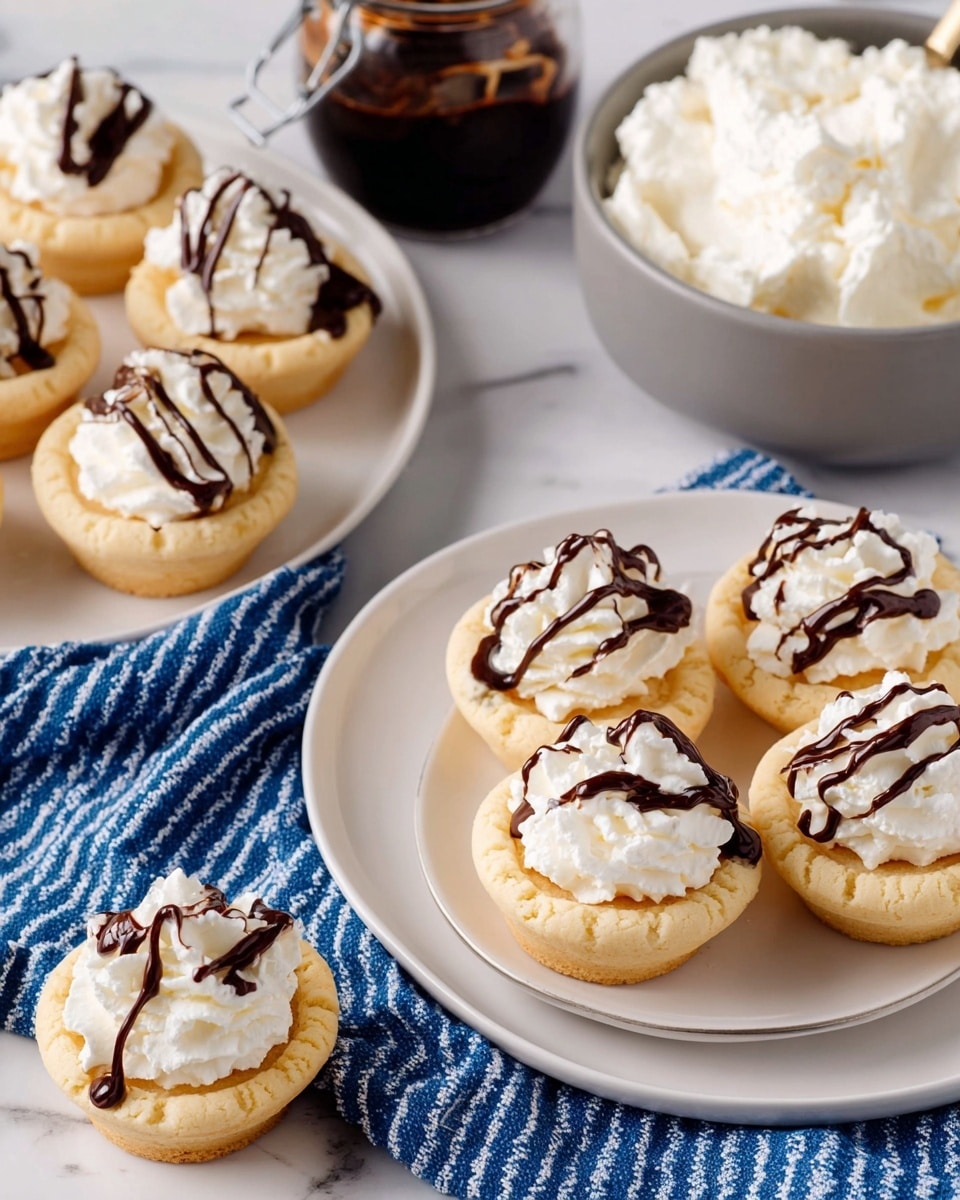 The image shows several mini cookie cups arranged on white plates and a white serving plate over a blue cloth with white stripes, all placed on a white marbled surface. Each cookie cup has two layers: the bottom layer is a light golden-brown baked cookie shaped like a small bowl with a smooth texture, and the top layer is a fluffy white whipped cream piped in a swirl pattern. The whipped cream is drizzled with dark brown chocolate sauce in thin, irregular lines. In addition, there is a gray bowl filled with white fluffy cream and a jar of dark chocolate sauce nearby. photo taken with an iphone --ar 4:5 --v 7