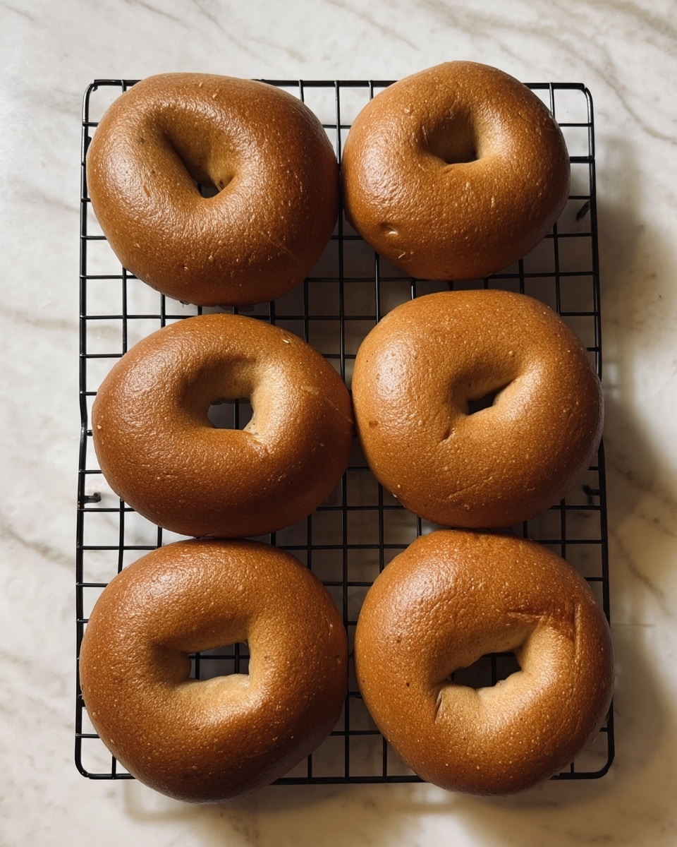 Six brown bagels with a smooth, shiny crust are placed in two neat rows of three on a black cooling rack. The bagels have a slight sheen, showing a well-baked surface with small imperfections and folds in the dough that give them a homemade look. The black rack contrasts with the white marbled texture below, highlighting the warm, golden-brown color of the bagels. The bagels are evenly spaced, and the lighting casts soft shadows that emphasize their round shape and thickness. photo taken with an iphone --ar 4:5 --v 7