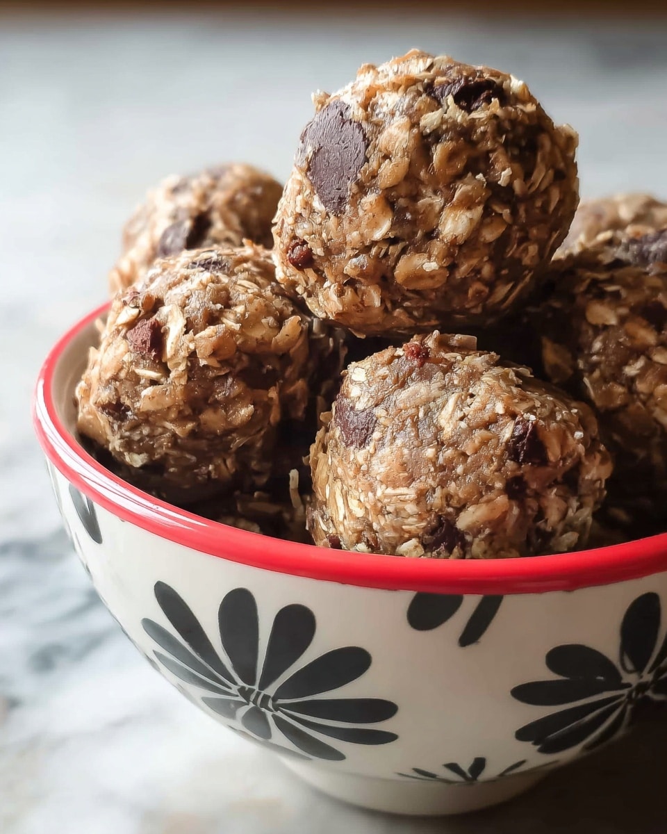Close-up of several round oatmeal cookie balls stacked in a white bowl with a red rim and black flower patterns on the side, each ball showing a rough texture with visible oats and dark chocolate chips mixed throughout, the background is a white marbled surface blurred softly, giving focus to the cookie balls' chunky and crumbly appearance, photo taken with an iphone --ar 4:5 --v 7