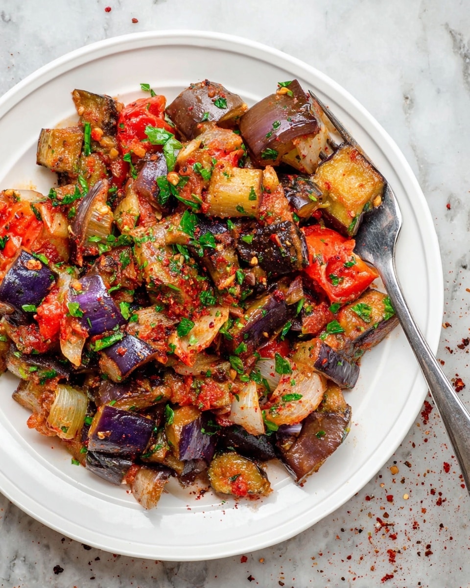 A white plate holds a colorful mix of cooked vegetable pieces including light brown and purple eggplants, red tomatoes, and translucent onions with bits of green parsley sprinkled on top. The vegetables are soft and slightly oily, with red seasoning flakes scattered throughout. A silver fork rests on the right side of the plate, partially holding some vegetables. The plate sits on a white marbled surface with some red and black seasoning flakes scattered around. photo taken with an iphone --ar 4:5 --v 7