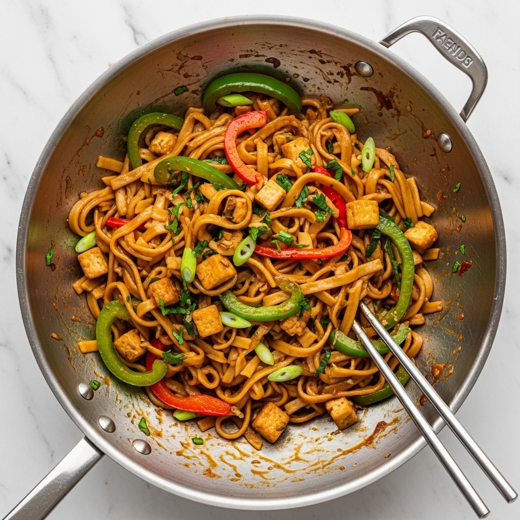 A shiny steel wok filled with thick flat noodles mixed with sliced green bell peppers, red bell peppers, and green onions, along with small cubes of tofu. The noodles and vegetables are coated with a glossy brown sauce, and small bits of herbs are scattered throughout. Metal chopsticks rest inside the wok, with the inside edges showing some sauce stains. The background is a white marbled texture. photo taken with an iphone --ar 4:5 --v 7